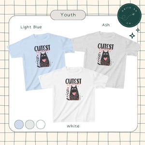 May include: Three youth-sized t-shirts in light blue, ash grey, and white, each featuring a black cat with a pink heart and the text "Cutest Valentine".