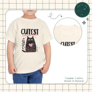 May include: A toddler-sized, natural colored t-shirt with a black cat graphic and the text "CUTEST Valentine".