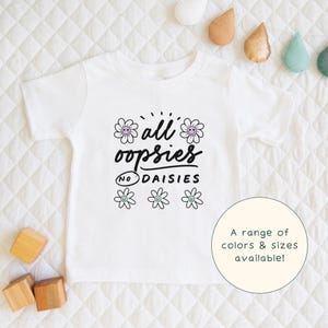 May include: White t-shirt with black text that says "all oopsies no daisies" with a daisy graphic. A range of colors and sizes are available.
