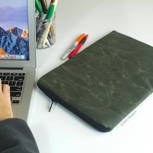 May include: A green laptop sleeve with a zipper closure. The sleeve has a textured, marbled pattern. The sleeve is made by Dory Designs.