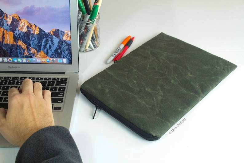 May include: A green laptop sleeve with a zipper closure. The sleeve has a textured, marbled pattern. The sleeve is made by Dory Designs.