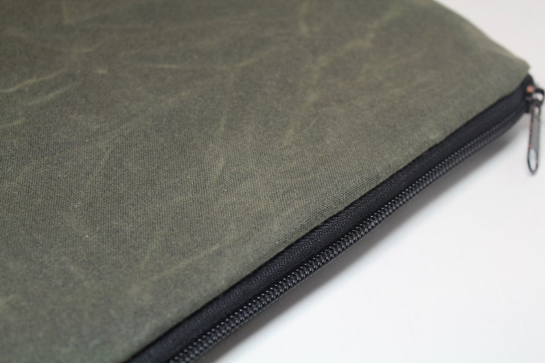 May include: A green canvas zippered pouch with a black zipper. The pouch is made of a durable, water-resistant material.
