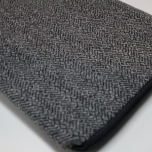Pode incluir: Uma capa para laptop cinza com um zíper preto e um padrão de espinha de peixe.