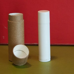 May include: Two empty containers for lip balm or other cosmetics. One is a brown cardboard tube with a white plastic cap. The other is a white plastic tube with a white plastic cap.