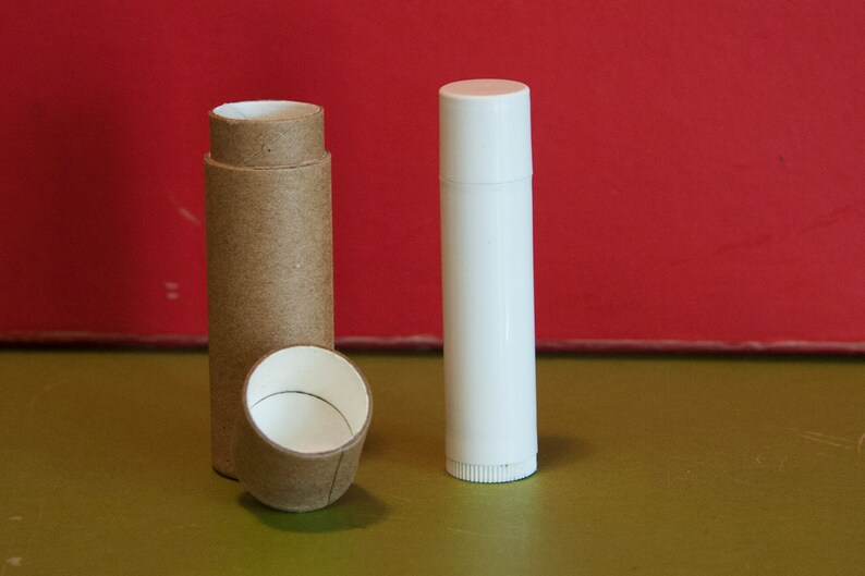 May include: Two empty containers for lip balm or other cosmetics. One is a brown cardboard tube with a white plastic cap. The other is a white plastic tube with a white plastic cap.
