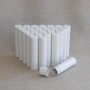 May include: A collection of white, cylindrical lip balm tubes arranged in a triangular shape. One tube is disassembled, showing the cap and the inside of the tube. The tubes are made of a speckled, matte white plastic.