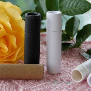 May include: Four cardboard tubes for lip balm or other small items. The tubes are in black, white, and brown. The tubes are on a pink and white patterned surface.