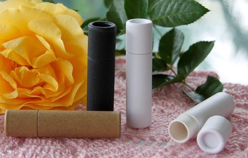 May include: Four cardboard tubes for lip balm or other small items. The tubes are in black, white, and brown. The tubes are on a pink and white patterned surface.