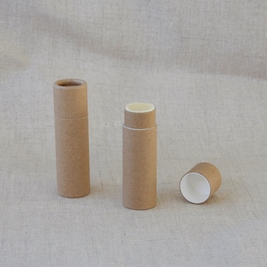 May include: Three brown cardboard tubes, two are closed and one is open, showing the white interior. The tubes are on a light brown fabric background.