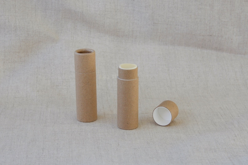 May include: Three brown cardboard tubes, two are closed and one is open, showing the white interior. The tubes are on a light brown fabric background.