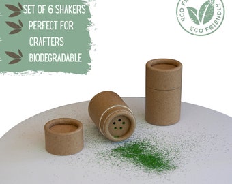 Puede incluir: Conjunto de seis agitadores de cartón marrón con polvo verde derramado sobre una superficie blanca. Los agitadores tienen un agujero en la parte superior para dispensar el polvo. El texto "ECO FRIENDLY" está impreso en un icono de hoja verde en un círculo.