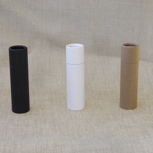 May include: Three cardboard tubes, one black, one white, and one brown, standing upright on a textured beige surface.