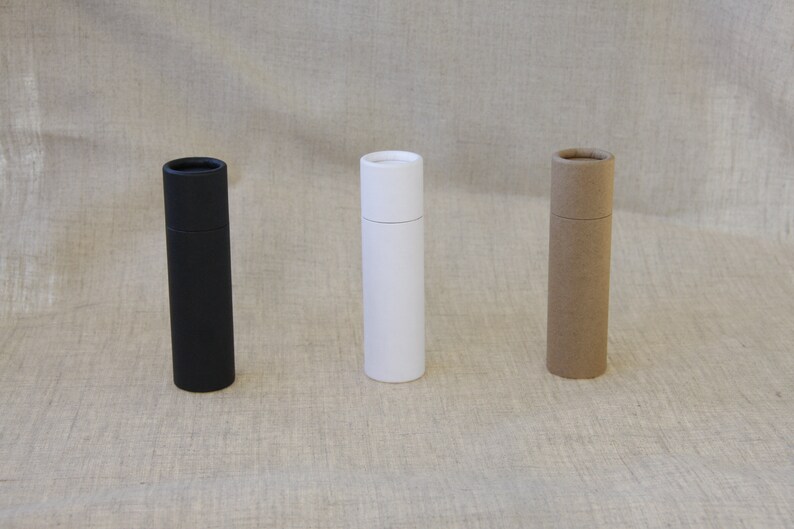 May include: Three cardboard tubes, one black, one white, and one brown, standing upright on a textured beige surface.