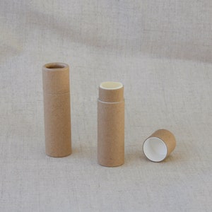 May include: Three brown cardboard tubes, two are closed and one is open, showing the white interior. The tubes are on a light brown fabric background.