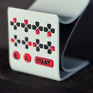 May include: A gray, curved desk organizer with a white front panel featuring red and black cross-shaped designs, and the letters "B", "A", and "START" in red. The organizer has a modern, minimalist design.