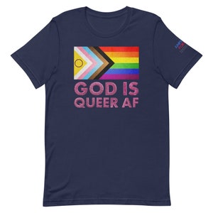Puede incluir: Camiseta azul marino con una bandera arcoíris del orgullo y el texto "GOD IS QUEER AF" en letras de purpurina rosa.