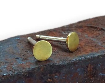 Puede incluir: Un par de pequeños pendientes redondos de color dorado. Los pendientes están hechos de latón y tienen un diseño simple y minimalista.