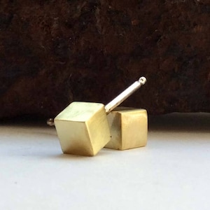 May include: Two gold cube earrings with a silver post. The earrings are small and delicate.
