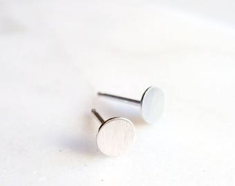 Op de afbeelding: Een paar zilveren oorbel studs met ronde, platte voorkanten. De oorbellen hebben een geborstelde afwerking.