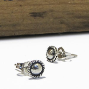 May include: A pair of silver stud earrings with a round, slightly raised center and a rope-like border.