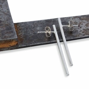 May include: A pair of silver bar stud earrings. The earrings are long and thin, with a simple, minimalist design.