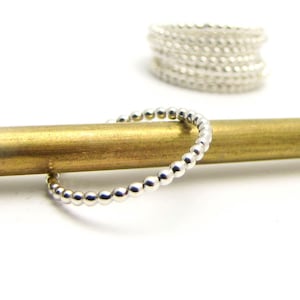 May include: A silver beaded ring on a brass rod. The ring is made of small, round beads that are evenly spaced.