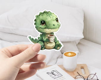 May include: A green cartoon dinosaur holding a cup of coffee with a smiley face on it. The dinosaur is sitting on a white background.
