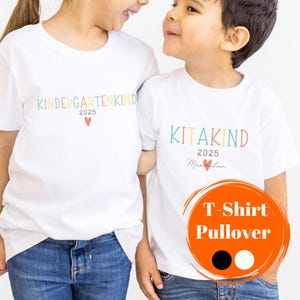 Könnte beinhalten: Zwei weiße T-Shirts mit buntem Text. Ein Shirt sagt "Kindergartenkind 2025" und das andere sagt "Kitakind 2025 Maximilian". Die Shirts werden von zwei Kindern in blauen Jeans getragen.