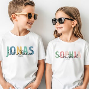 Einschulung T-Shirt 2026 personalisiert mit Name, Schulkind Shirt Mädchen, Tshirt zum Schulstart Junge, Einschulungsshirt Weiß Regenbogen