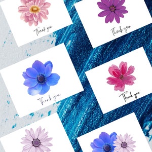 May include: A collection of six white cards with floral designs and the words "Thank you" in black script. The flowers are in shades of pink, purple, and blue. The background is a textured blue and white surface.