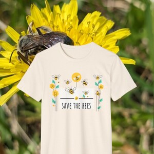 May include: A cream-colored t-shirt with a graphic of bees flying around a yellow flower and the text "SAVE THE BEES".