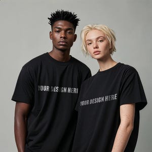 May include: Two people wearing black t-shirts with the text "YOUR DESIGN HERE" in silver. The shirts are short-sleeved and appear to be made of a soft material. The background is a solid, neutral gray.