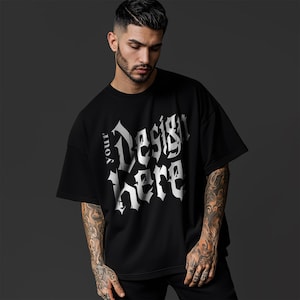 May include: Black oversized t-shirt with the text "Your Design Here" in a gothic font. The shirt has short sleeves and a relaxed fit. The model is wearing black pants.