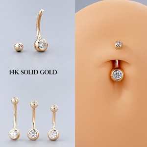 May include: Three gold belly button rings with clear gemstones. The rings are shown on a white background. 14K SOLID GOLD.