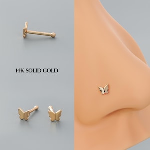 Könnte beinhalten: Ein goldener Nasenring in Form eines Schmetterlings aus 14 Karat massivem Gold. Der Ring wird an der Nase eines Models gezeigt.