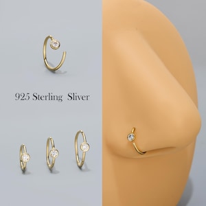 Könnte beinhalten: Goldfarbene Nasenringe mit einem kleinen, klaren Edelstein. Das Bild zeigt drei Ringe in verschiedenen Größen sowie einen an einer Nase. Der Text "925 Sterling Sliver" ist ebenfalls sichtbar.