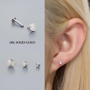 May include: A collection of 14K solid gold earrings with a sunburst design. The image shows several sizes of the earrings, including one worn on an ear. The text "14K SOLID GOLD" is displayed.