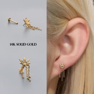 May include: Gold earrings with a cannabis leaf design and chain dangles. The image shows the earrings in different views, including one worn in an ear. The text "14K SOLID GOLD" is visible.