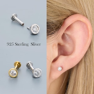 May include: A collection of silver and gold-toned stud earrings with clear, round gemstones. One earring is shown in a person's ear. The text "925 Sterling Sliver" is displayed in the image.