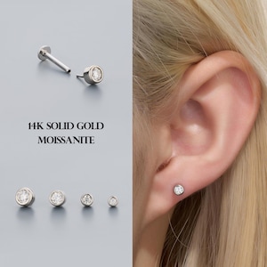 May include: A collection of 14K solid gold moissanite earrings in various sizes. One earring is shown separately with a post. The text "14K SOLID GOLD MOISSANITE" is displayed in the image.