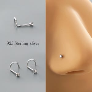 May include: Silver nose studs with a small, clear gemstone. The image shows three studs and a close-up of one stud on a nose. The text "925 Sterling sliver" is also visible.
