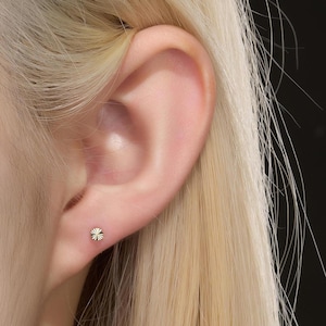 K&ouml;nnte beinhalten: Nahaufnahme eines Ohrs mit einem kleinen, goldfarbenen Ohrstecker. Der Ohrring hat ein Sternmuster. Die Person hat blondes Haar.
