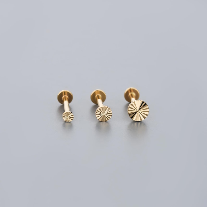 K&ouml;nnte beinhalten: Drei goldfarbene Ohrringe mit flacher R&uuml;ckseite und Sonnenstrahl-Design. Die Ohrringe sind in verschiedenen Gr&ouml;&szlig;en erh&auml;ltlich, mit einer kleinen, mittleren und gro&szlig;en Option. Die Ohrringe befinden sich auf einem grauen Hintergrund.