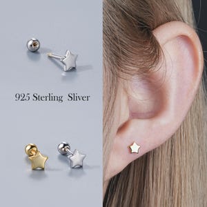 Könnte beinhalten: Ohrstecker in Sternform in Silber und Gold. Das Bild zeigt eine Nahaufnahme der Ohrringe, von denen einer am Ohr getragen wird. Der Text "925 Sterling Sliver" ist zu sehen. Kleines, filigranes Design.