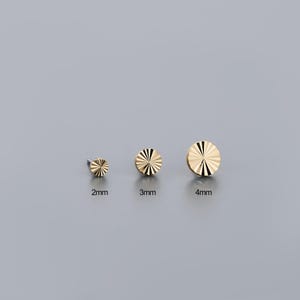 K&ouml;nnte beinhalten: Drei goldfarbene Ohrstecker mit radialem Design. Die Ohrringe haben einen Durchmesser von 2 mm, 3 mm und 4 mm. Die Ohrstecker werden auf grauem Hintergrund pr&auml;sentiert.