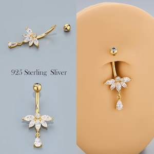 Könnte beinhalten: Goldfarbene Bauchnabelpiercings mit klaren, funkelnden Edelsteinen. Ein Ring hat ein geschwungenes Design mit einem Blumencluster und einem Tropfen-Edelstein. Der Text "925 Sterling Sliver" ist sichtbar.