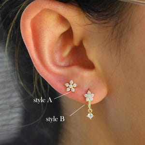 Puede incluir: Dos estilos de pendientes con diseño de flor. El estilo A es un pendiente de flor individual. El estilo B es un pendiente de flor colgante con una sola piedra que cuelga de la parte inferior.