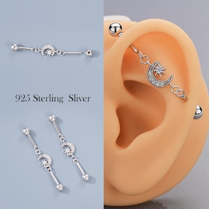 May include: Silver industrial barbell and dangling earrings featuring a crescent moon and star design. The earrings and barbell are adorned with small, sparkling stones. The text "925 Sterling Sliver" is visible in the image.