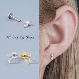 May include: A collection of silver and gold-toned earrings with clear, teardrop-shaped and round gemstones. The earrings are shown in various arrangements, including a close-up of one in a person's ear. The text "925 Sterling Sliver" is also visible.