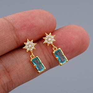 May include: Gold star-shaped earrings with clear cubic zirconia stones and a dangling rectangular blue gemstone.